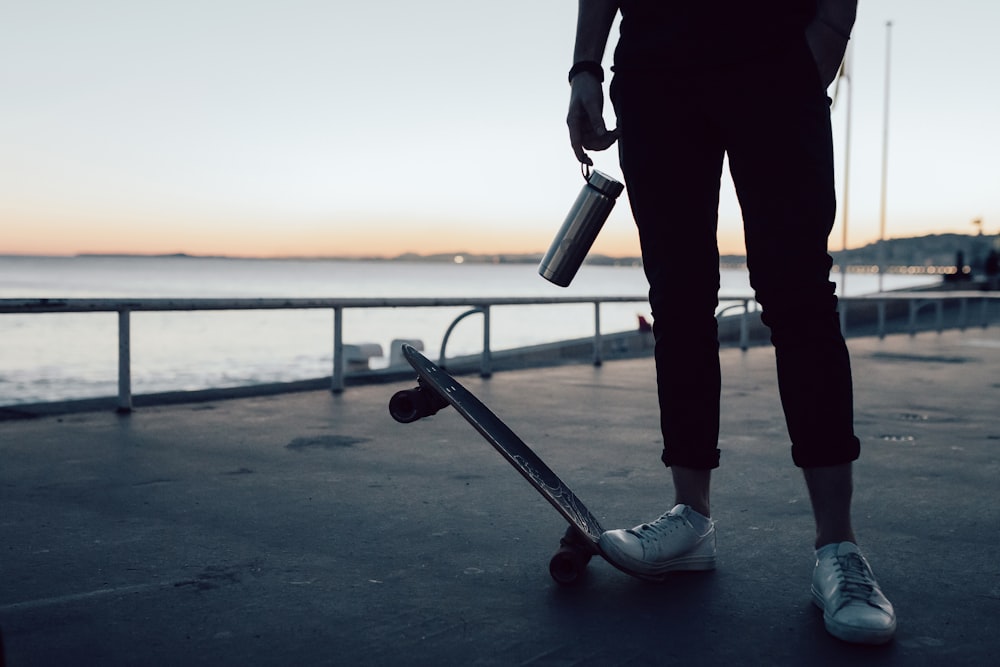 hombre en chaqueta negra y pantalones sosteniendo patineta