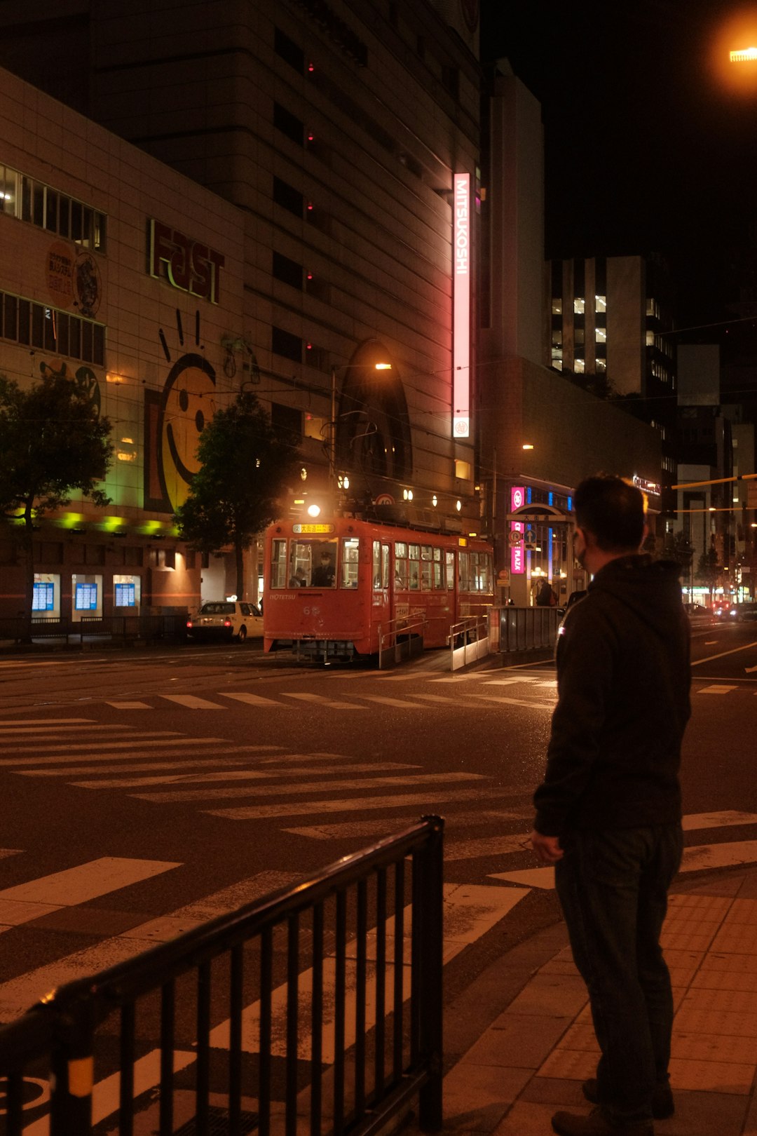 man in gray jacket walking on pedestrian lane during night time