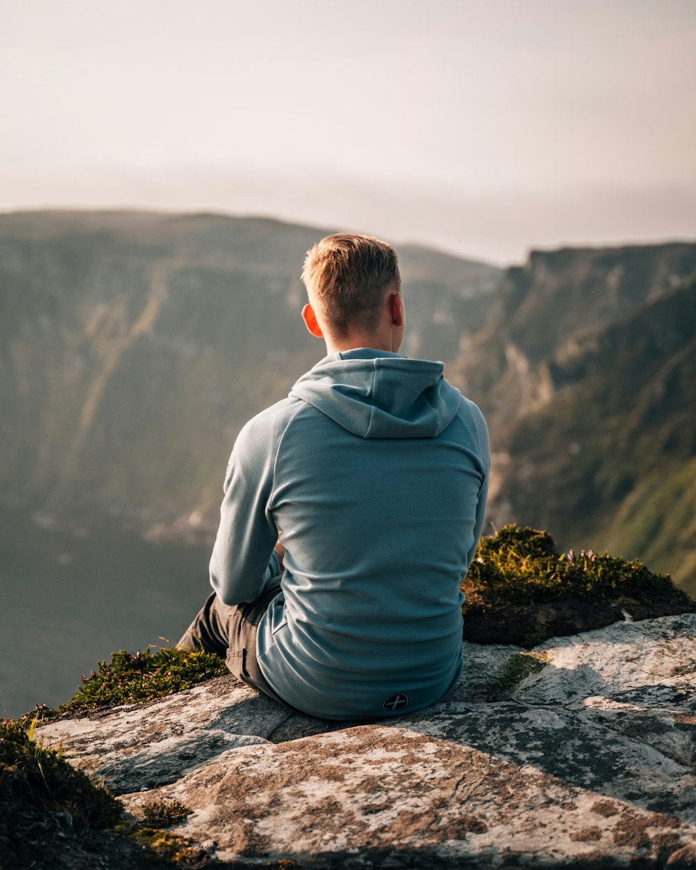 man in blue hoodie sitting on rock