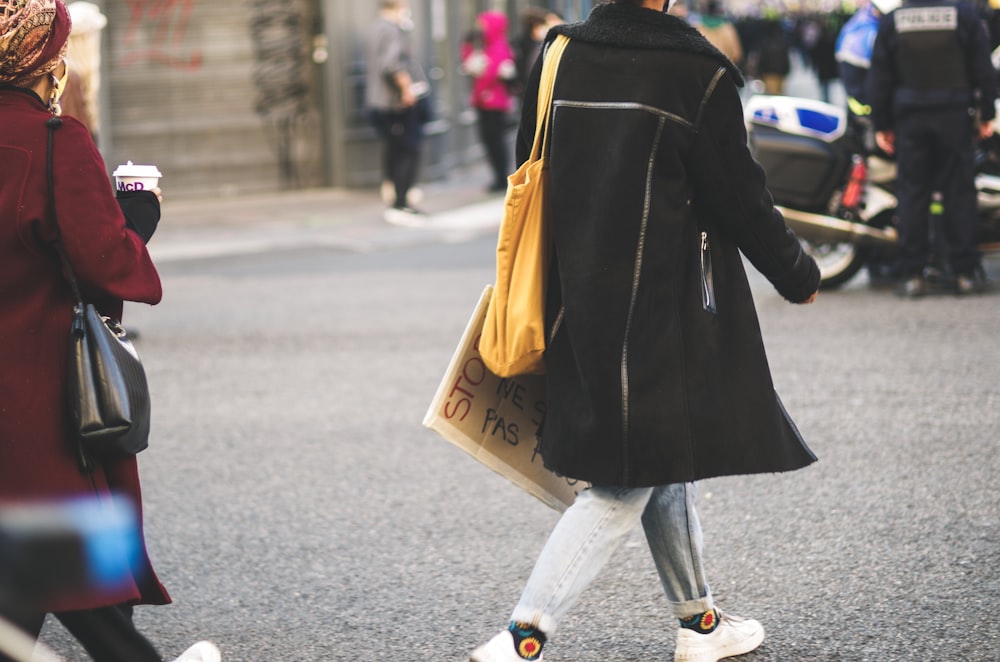 woman in black coat and white pants walking on street