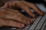 Close-up view of hands typing on a computer keyboard. The fingers are poised over the keys, suggesting active engagement with typing or data entry.
