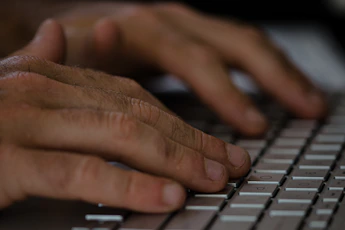 Close-up of hands typing on a keyboard with website analytics displayed on screen.