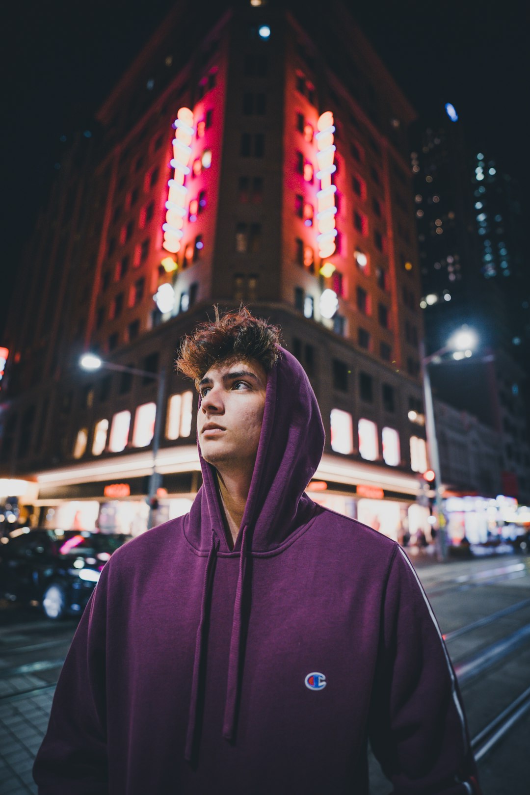 man in purple hoodie standing near building during nighttime