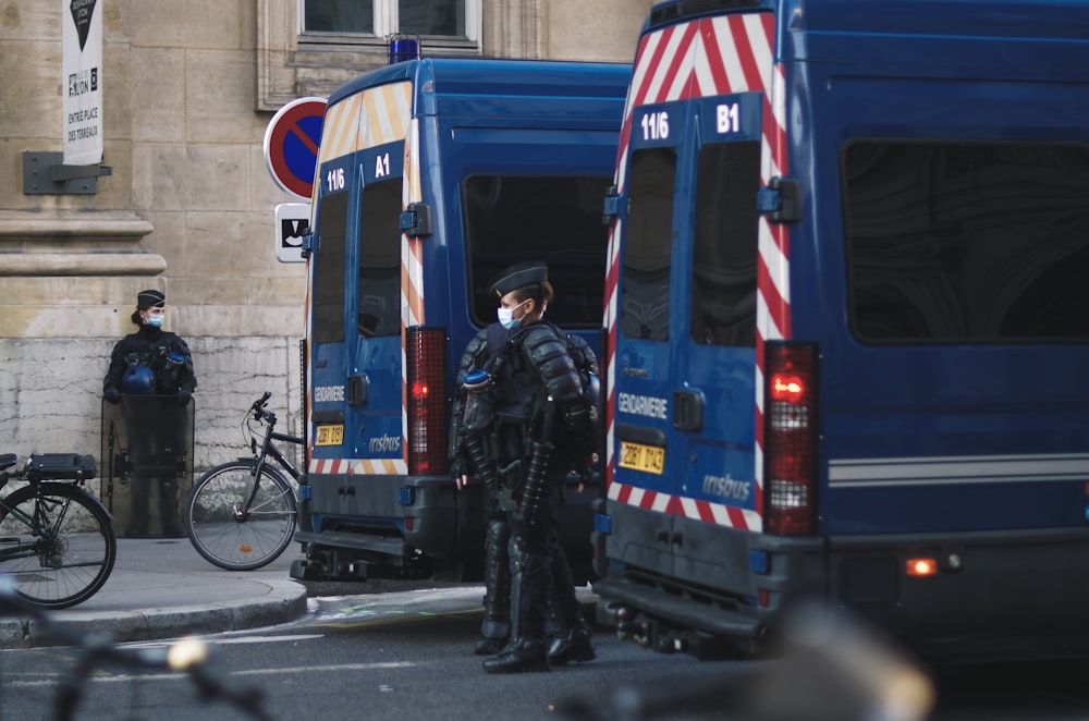 man in black jacket standing beside blue and white bus during daytime