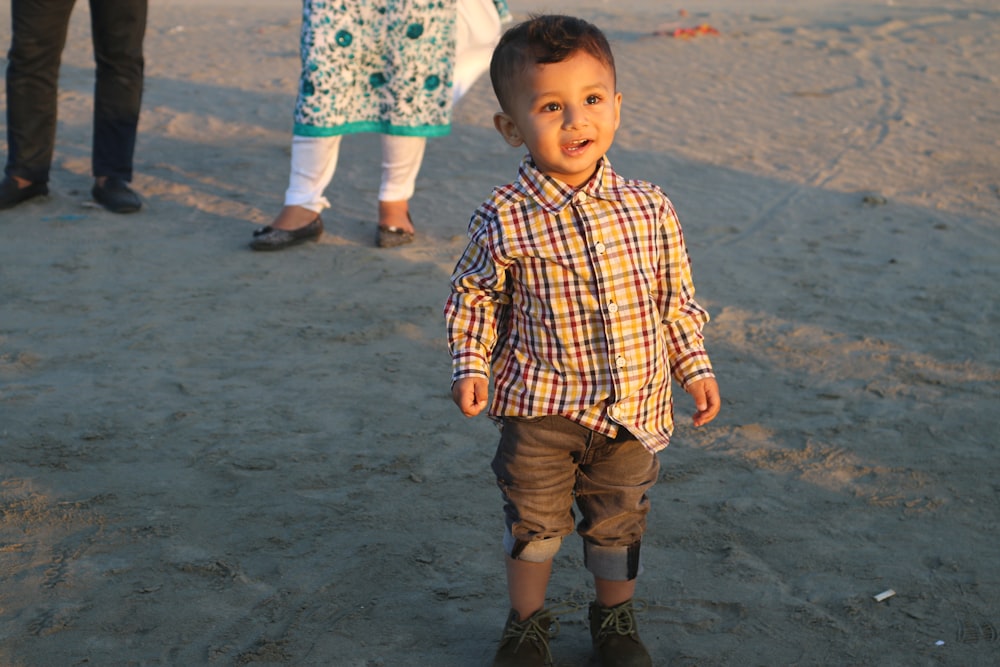 boy in yellow and black plaid button up shirt standing on beach during daytime