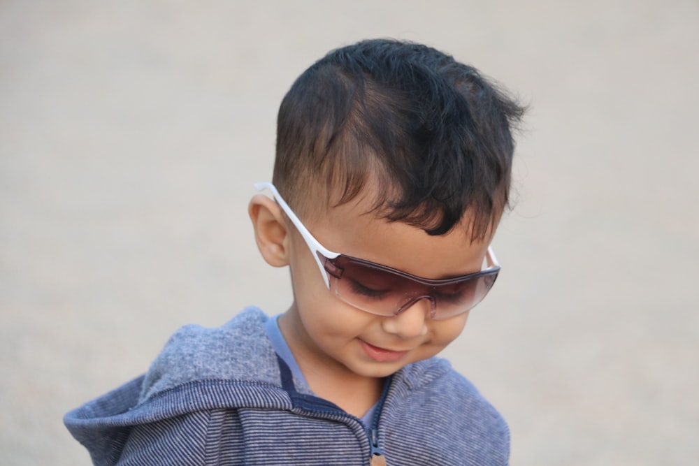 Niño con camisa de cuello a rayas azules y blancas con gafas de sol de montura blanca