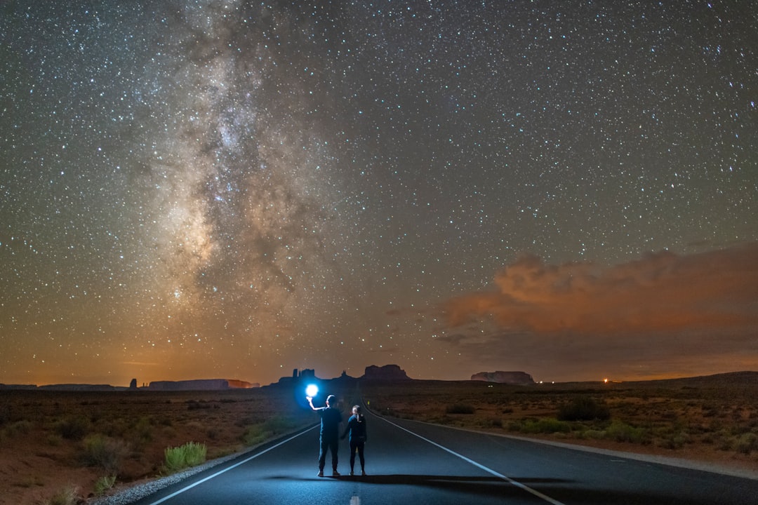 man in black jacket and blue denim jeans standing on road under starry night