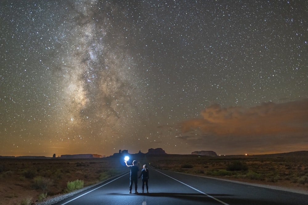 man in black jacket and blue denim jeans standing on road under starry night