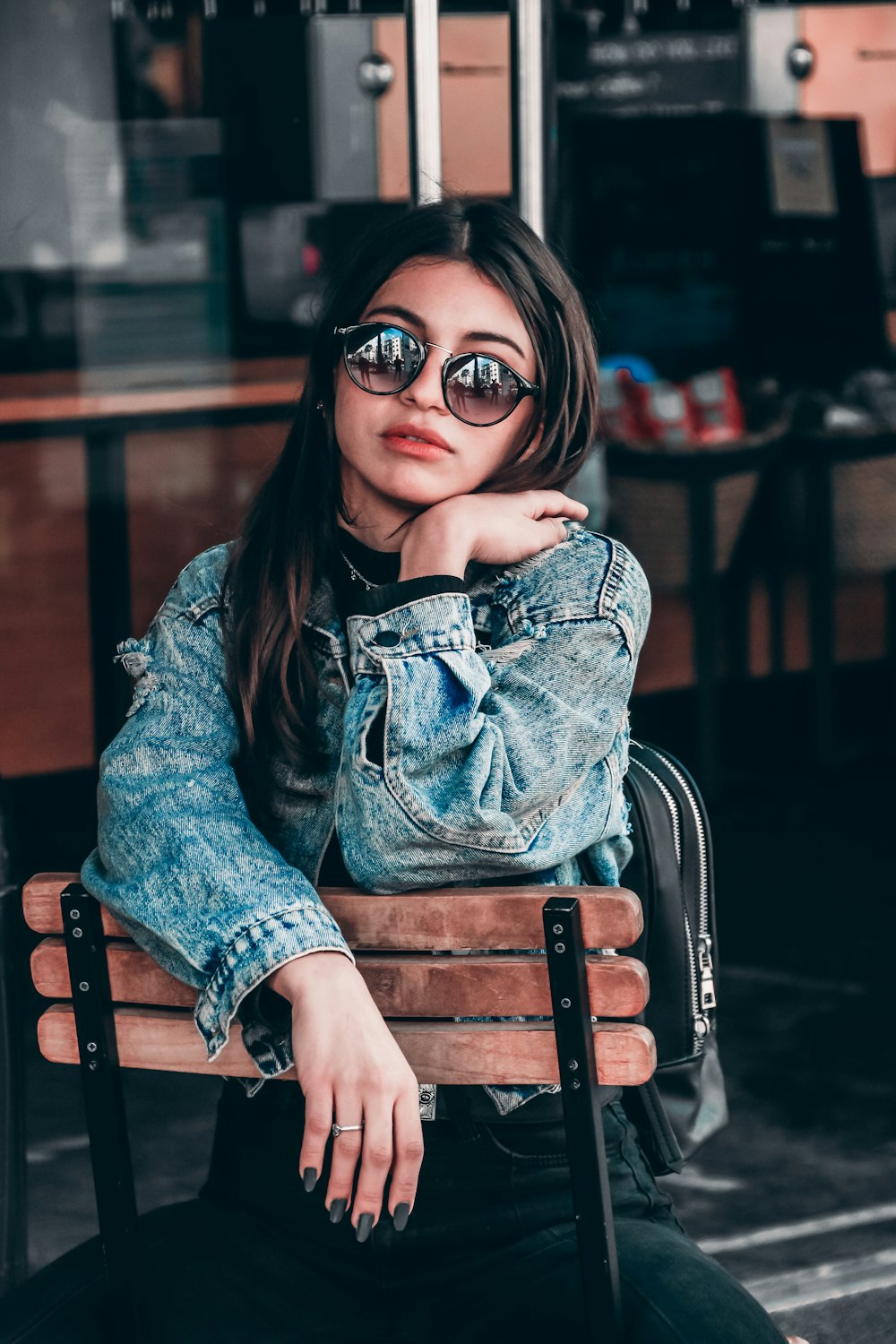 woman in blue denim jacket sitting on brown wooden chair