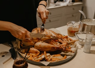 person holding stainless steel fork and bread knife slicing grilled meat on white ceramic plate