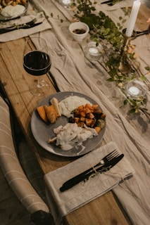 An inviting wooden table set for two with linen napkins, flickering candles, and a serving bowl filled with golden roasted vegetables.