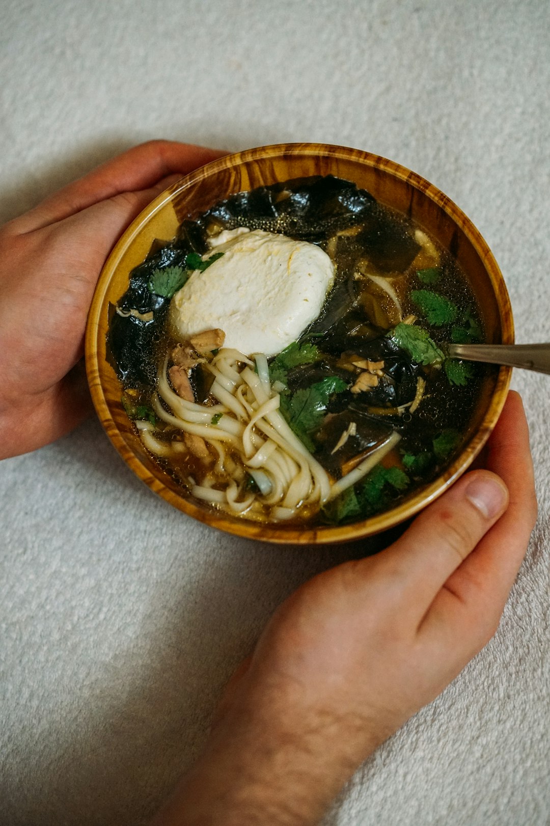 person holding brown and black ceramic bowl with soup