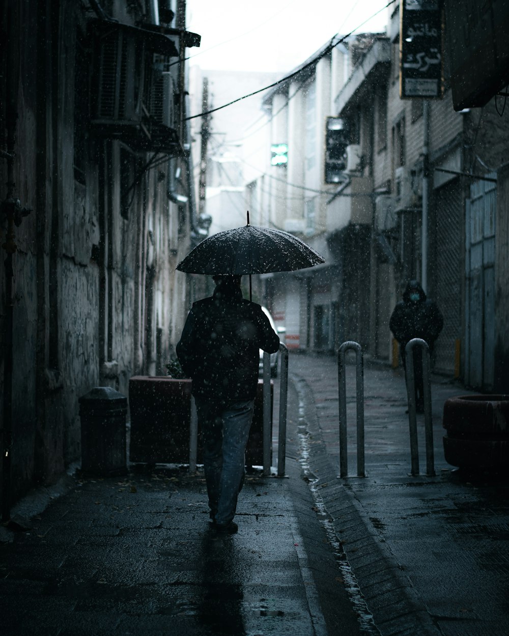 검은 재킷과 바지를 입은 사람이 낮 동안 보도를 걷고 있는 우산을 들고 있다