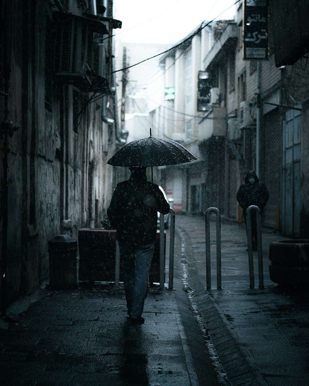 person in black jacket and pants holding umbrella walking on sidewalk during daytime