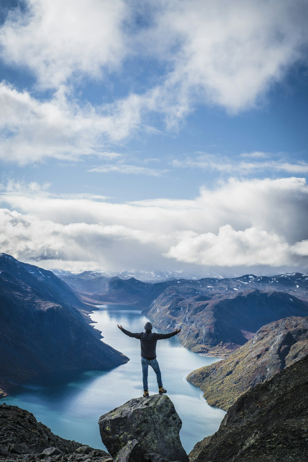 person standing on rock formation near mountains under white clouds during daytime