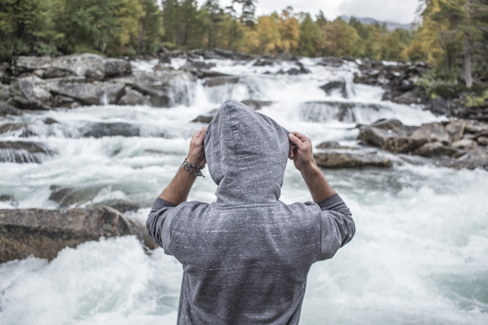 woman in gray long sleeve shirt standing on rock near river during daytime