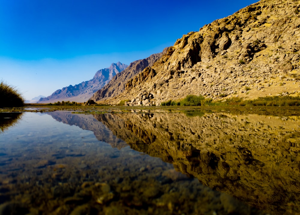 brown and green mountain beside lake under blue sky during daytime