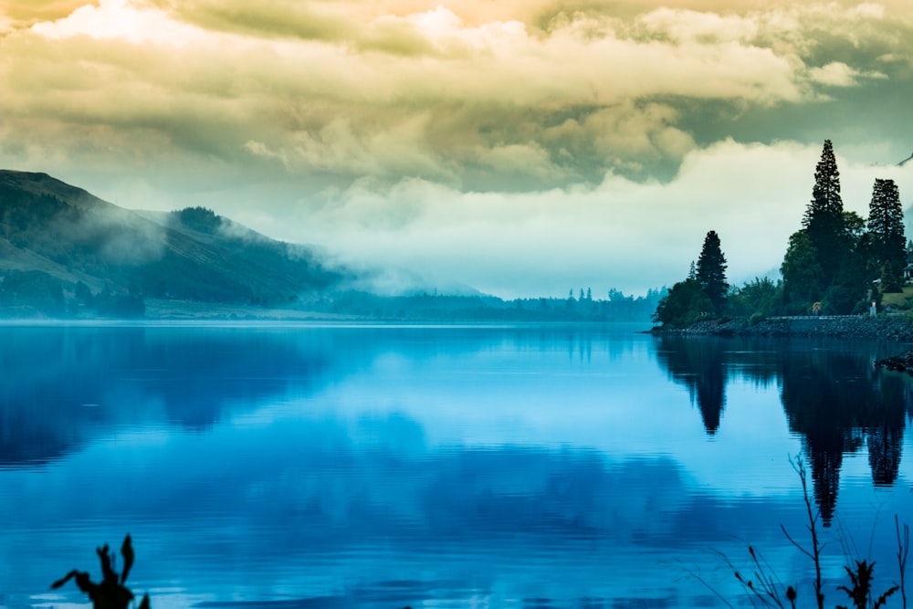 body of water near mountain under cloudy sky during daytime