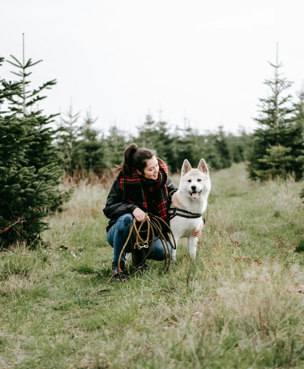 woman in black jacket sitting on white dog on green grass field during daytime