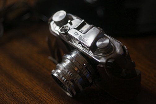 A vintage camera with a metallic body and mechanical dials sits on a wooden surface, casting a nostalgic and timeless aura.