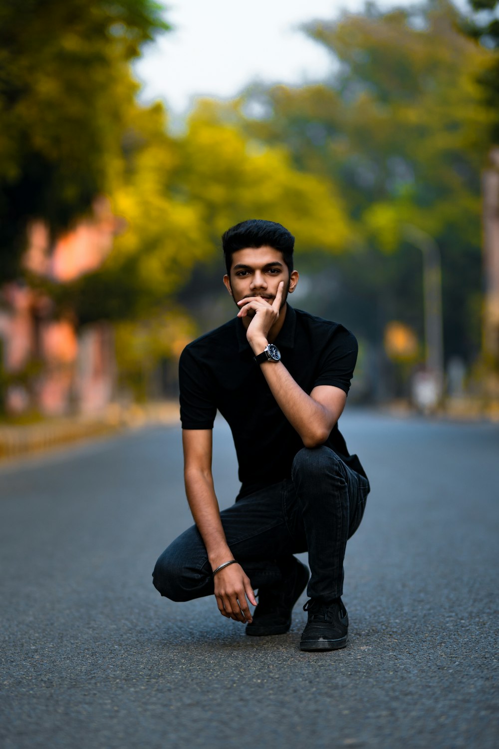 man in black crew neck t-shirt and black pants sitting on gray asphalt road during