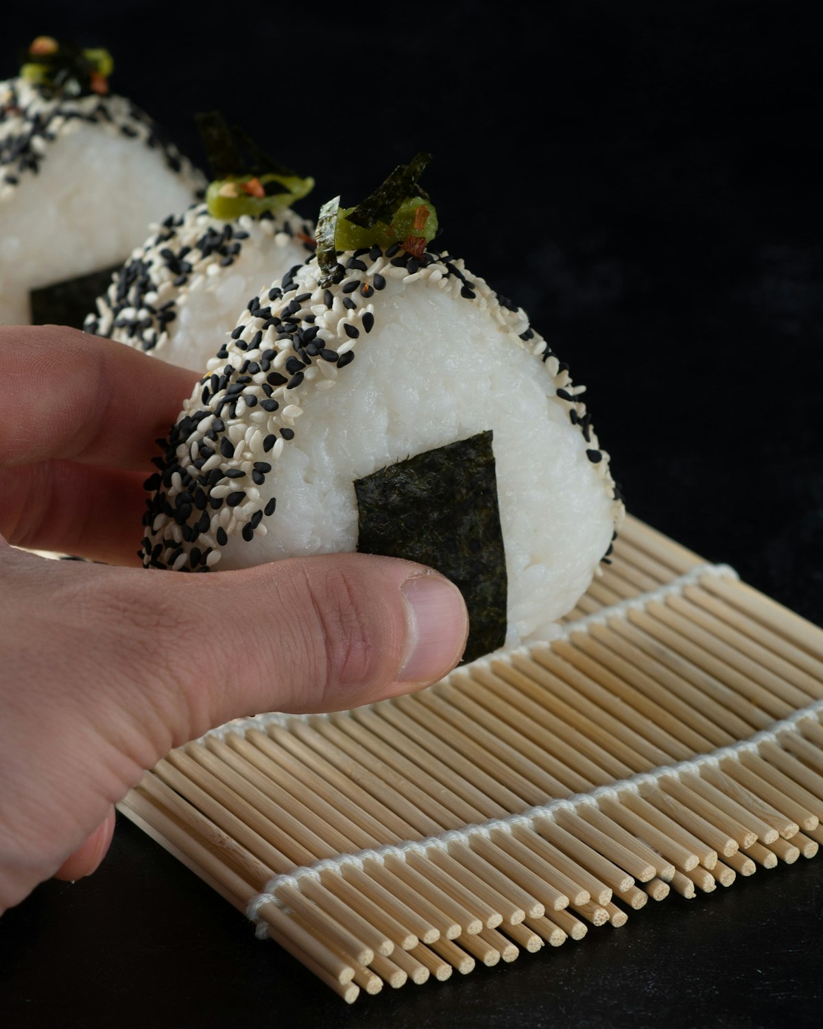 A hand holding a freshly made Japanese onigiri rice ball wrapped in nori seaweed
