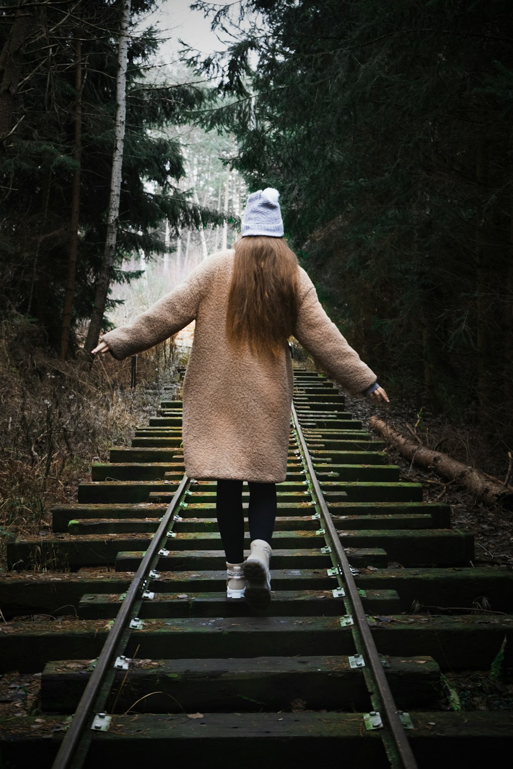 woman in brown coat walking on wooden bridge