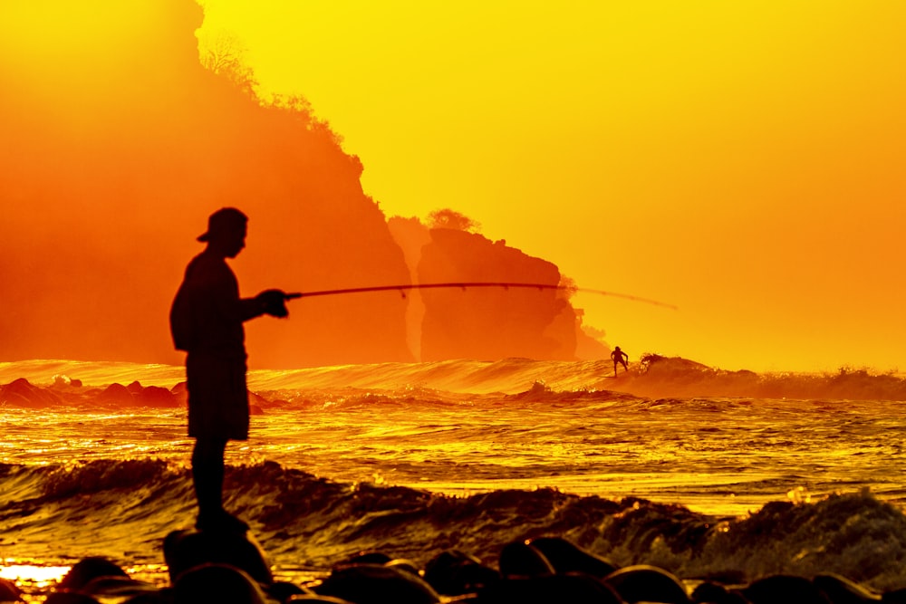 silhouette of man holding fishing rod during sunset