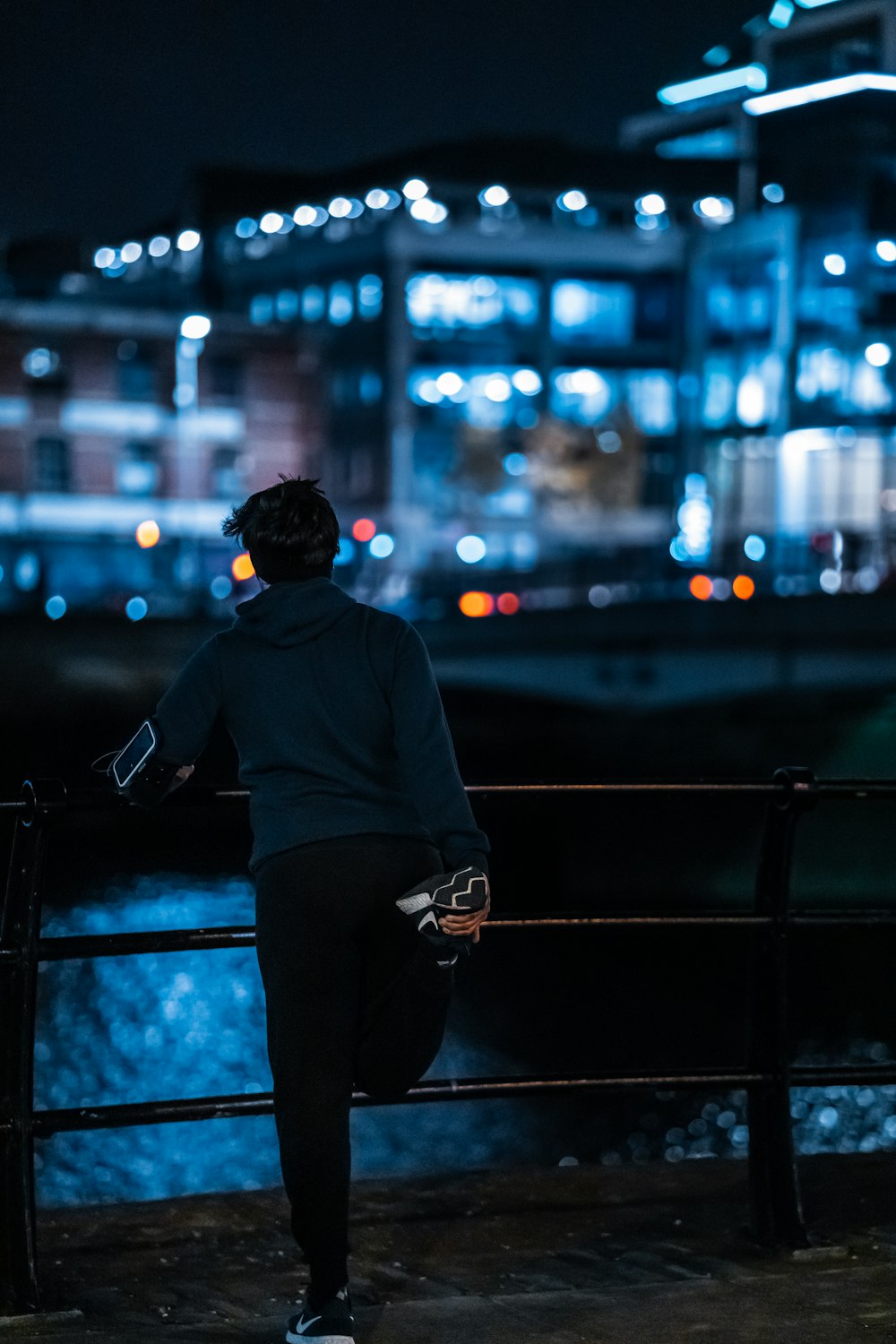 man in gray long sleeve shirt and black pants sitting on black metal fence during night