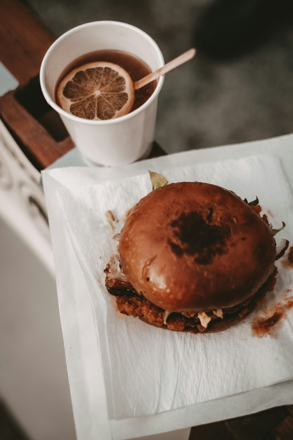 burger on white paper beside white disposable cup