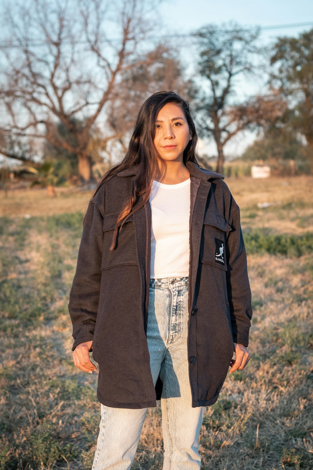 woman in brown coat standing on brown grass field during daytime