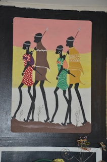 A painting depicts four slender figures walking in profile across a simple landscape. The figures wear traditional clothing with colorful patterns: red with white spots, brown and purple, green with white dots, and yellow with geometric designs. Each holds a spear and carries a round object on their back. The background transitions from pink to yellow, representing a sunset or sunrise.