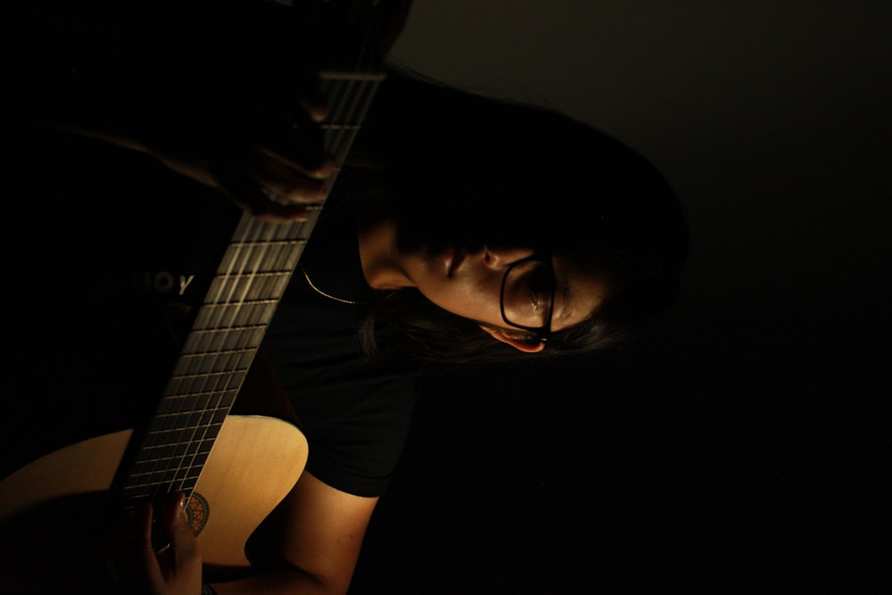 woman in black framed eyeglasses playing guitar