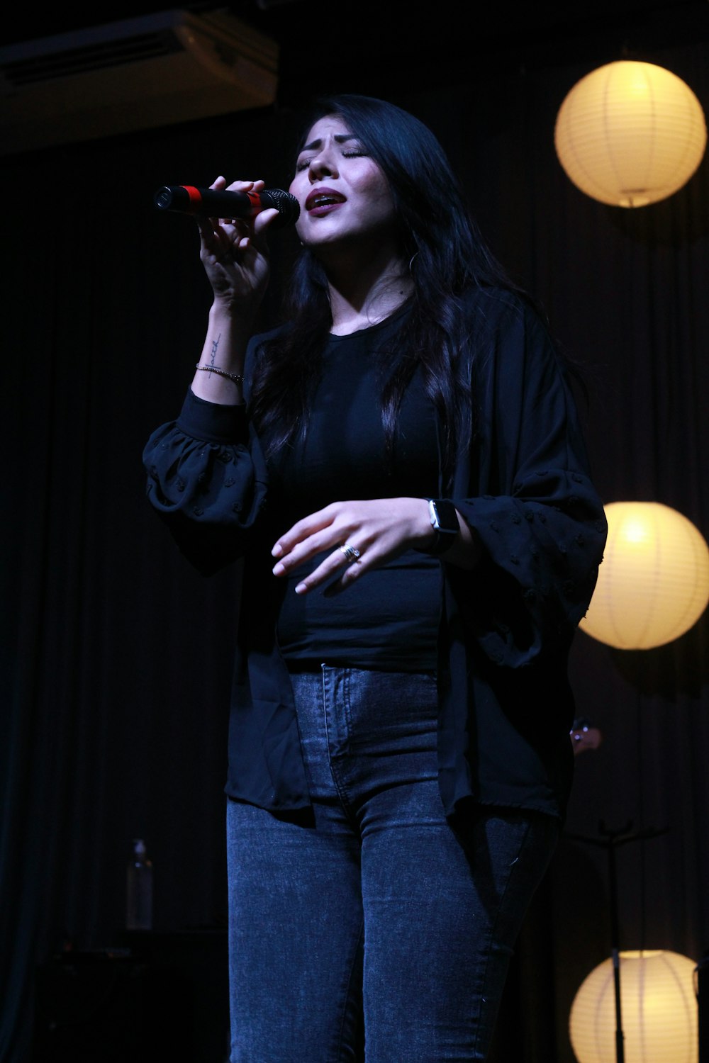woman in black leather jacket and blue denim jeans holding microphone