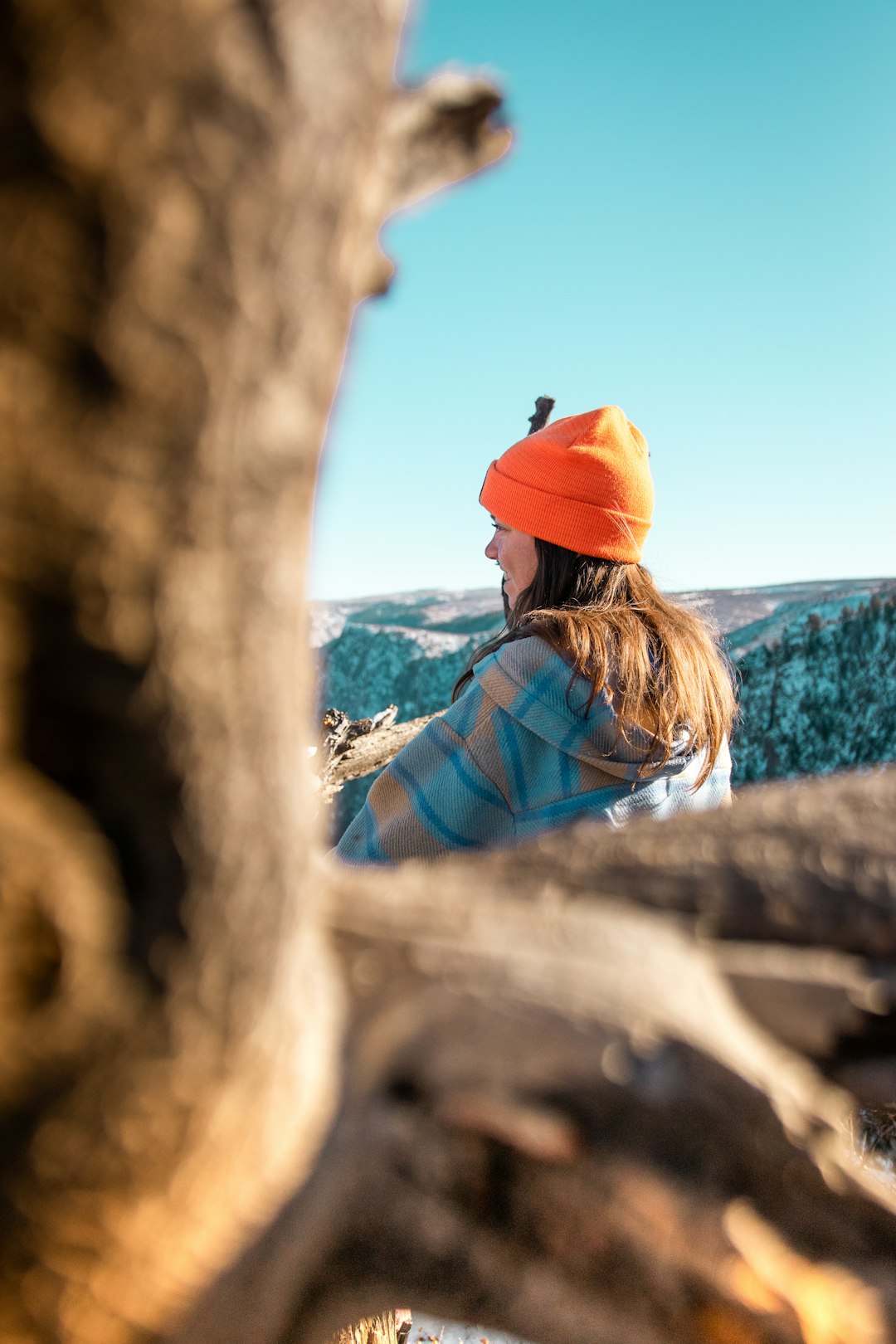 woman in orange cap and blue and white plaid dress shirt leaning on brown rock