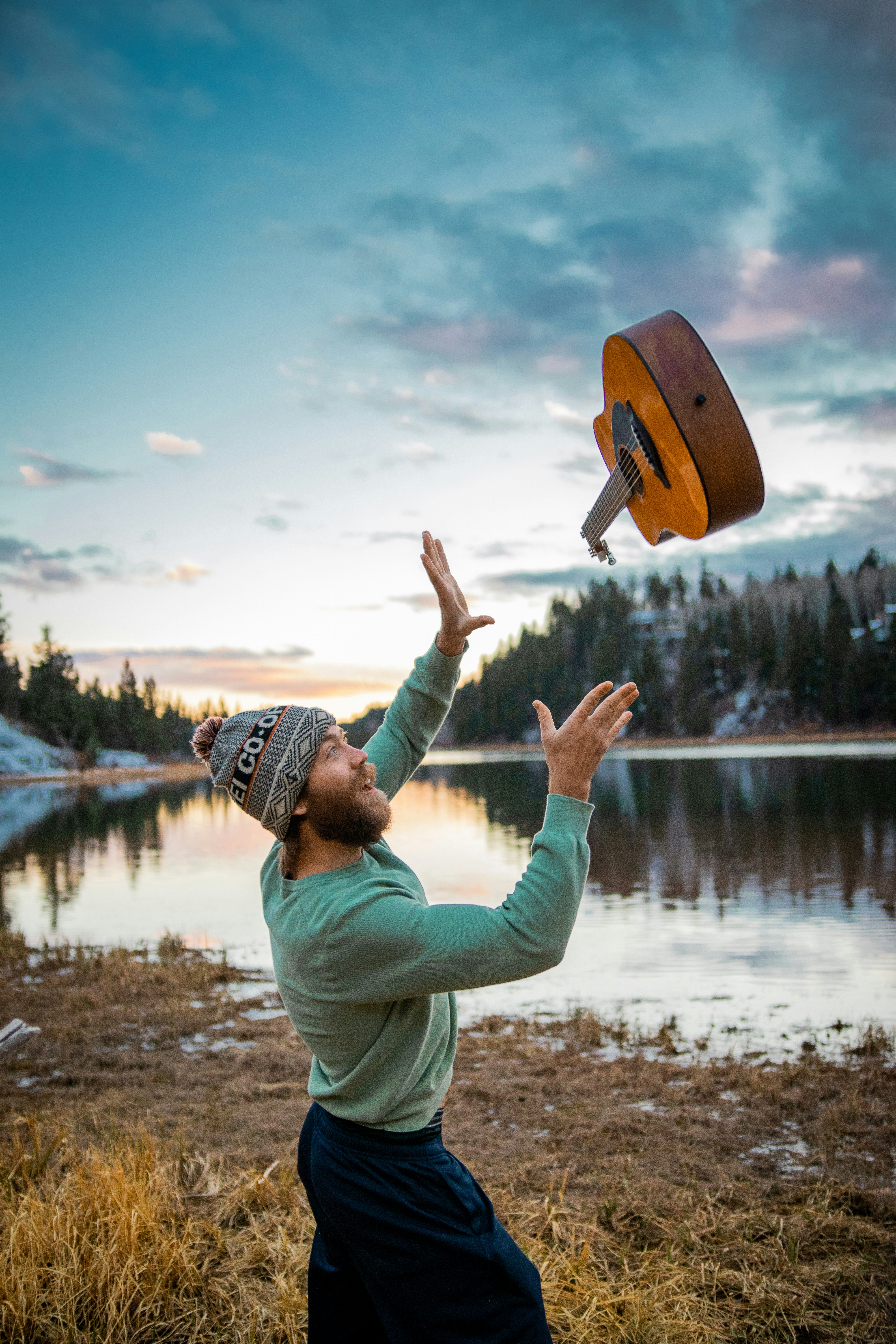 man in green jacket and brown hat standing near lake during daytime