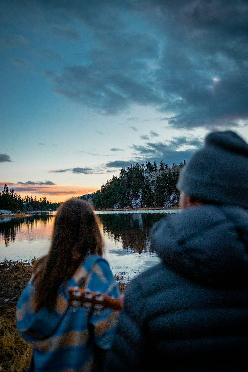 woman in blue hoodie sitting on rock near lake during daytime