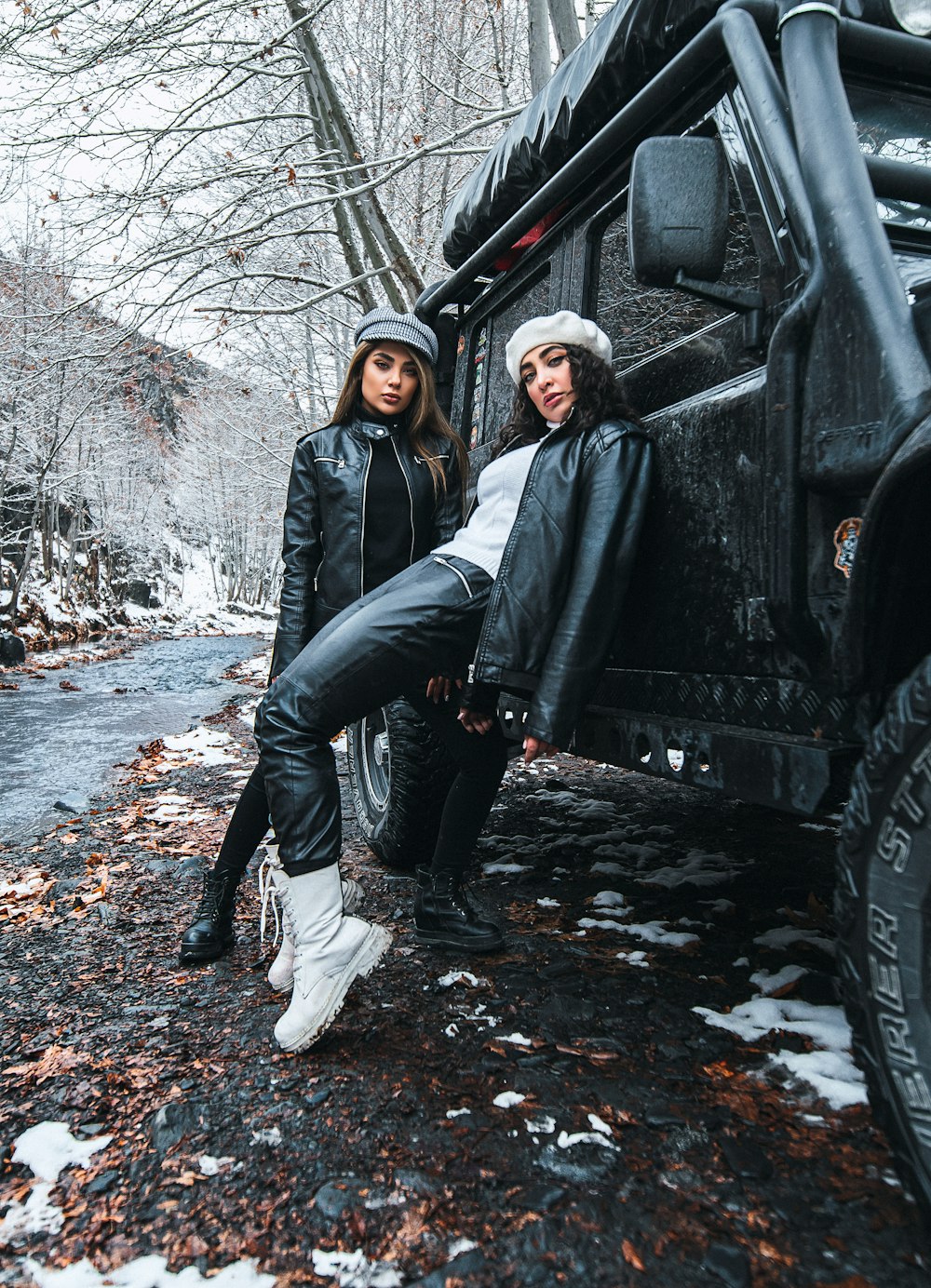 woman in black leather jacket and black pants leaning on black car