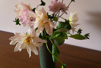 A delicate bouquet of dahlias and wildflowers in antique pink and warm orange tones on a rustic wooden table.