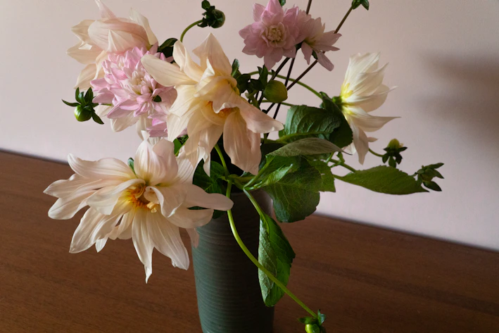 A soft, elegant bouquet of neutral-toned flowers arranged with delicate greenery on a rustic wooden table.