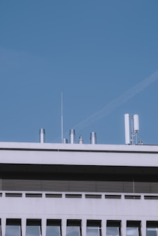 The image depicts the top portion of a modern building with several silver-colored ventilation pipes and an antenna against a clear blue sky.