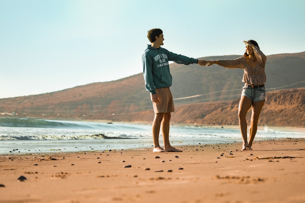 man in blue long sleeve shirt and brown shorts walking on beach shore during daytime