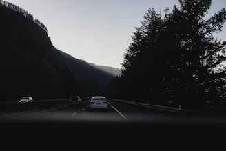 A panoramic view of a Yoocabs vehicle convoy making its way through a winding mountain highway during golden hour.