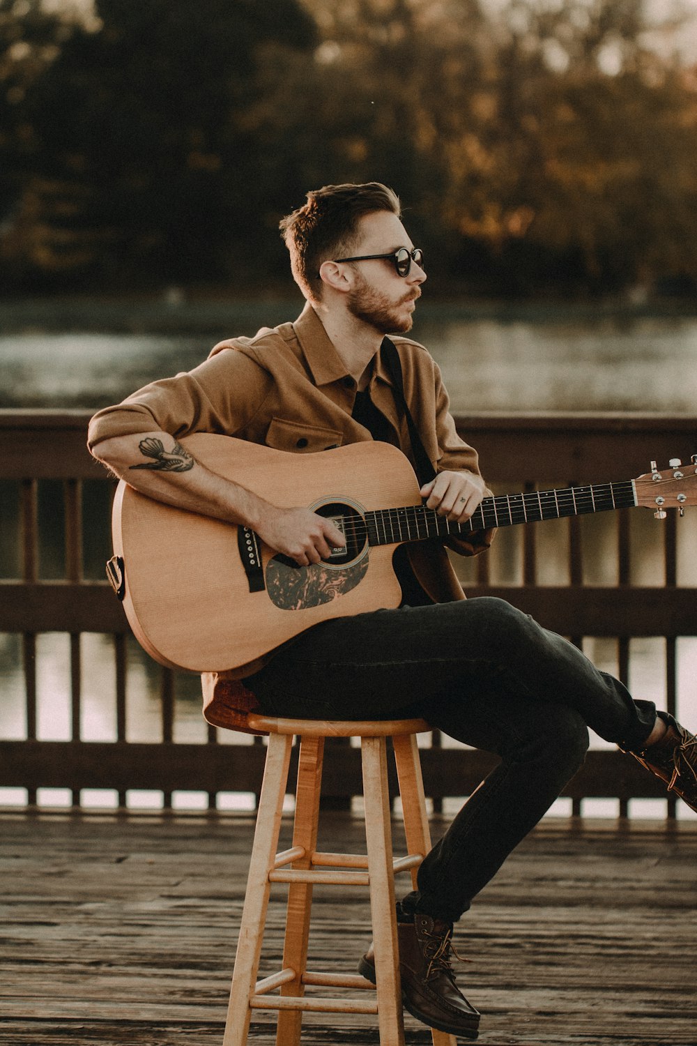 man in brown coat and black pants sitting on brown wooden chair playing brown acoustic guitar