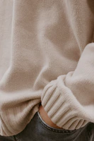Close-up of a soft beige knitted sweater with delicate ribbing detail.
