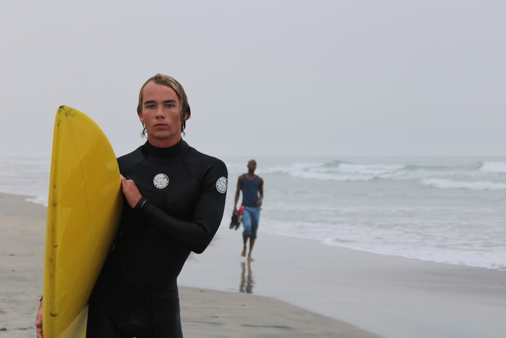 homem na camisa preta de manga comprida segurando a prancha de surf amarela