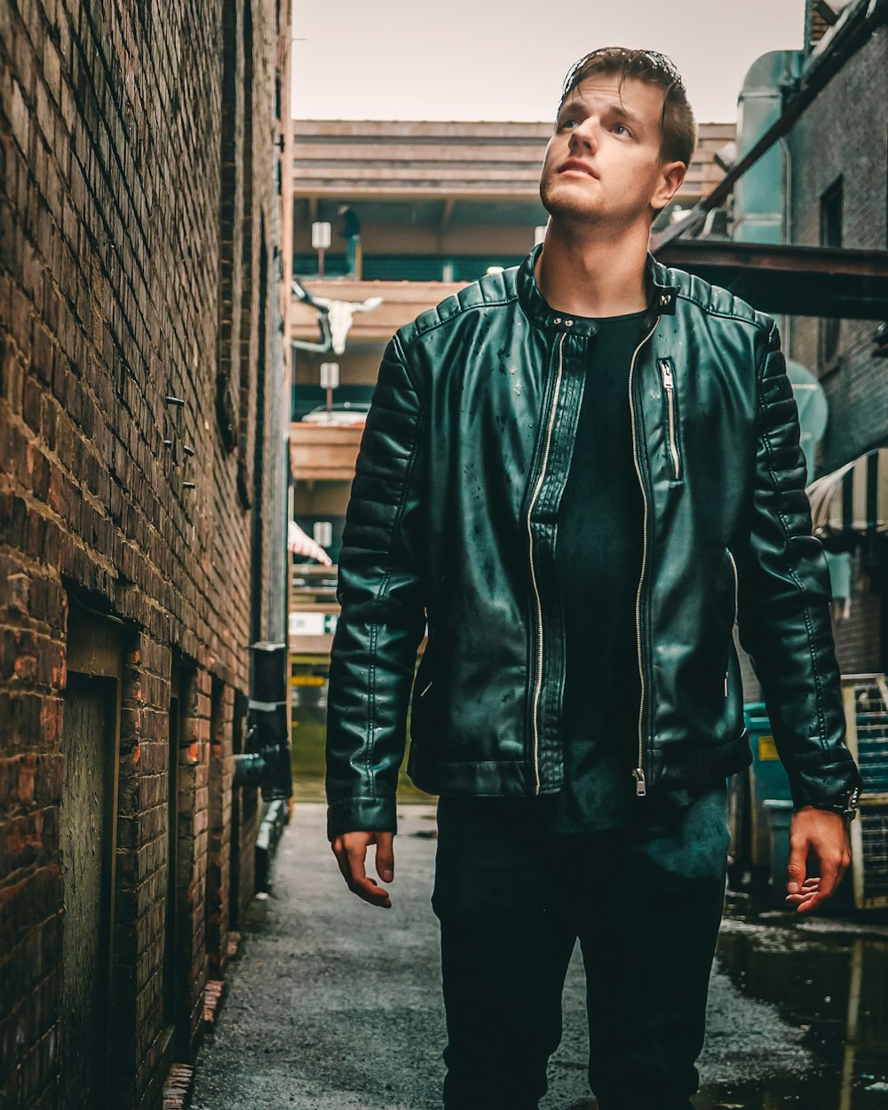 man in green zip up jacket standing beside brick wall