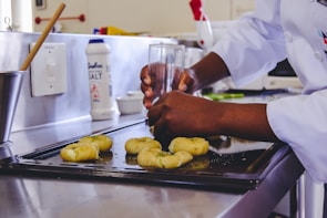 Bakers in white uniforms carefully shaping dough on a large stainless steel table.