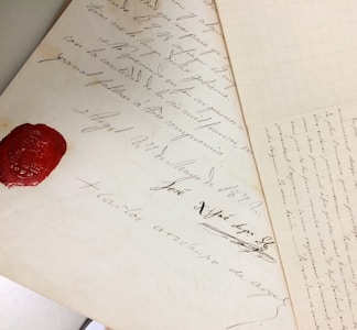 Antique handwritten documents with elegant cursive script are displayed, featuring a prominent red wax seal on one of the pages.