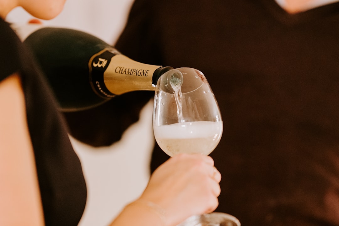 person holding black labeled bottle pouring on clear glass, Pouring Champagne into a glass